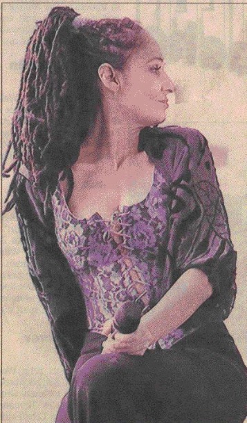 Sandra Kreisler mit langen Dreadlocks im violetten Spitzenoberteil, sitzend mit Mikrofon