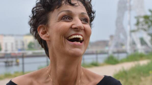 Sandra Kreisler lacht, im Hintergrund ein Fluss und Häuser
